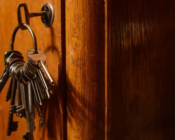 Un trousseau de clés pend à une serrure sur une porte en bois. Ces clés symbolisent la sécurité et la protection, rappelant les lois anti squat.