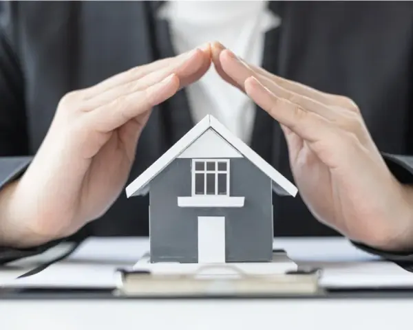 Mains protégeant une maquette de maison, symbolisant la **garantie de bon fonctionnement** et la sécurité de votre investissement immobilier.