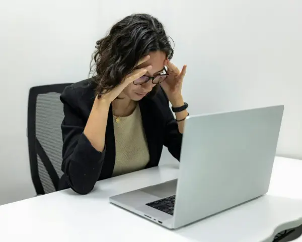Femme stressée devant son ordinateur, les mains sur les tempes. Une situation difficile, peut-être un licenciement pendant arrêt maladie pour dépression.