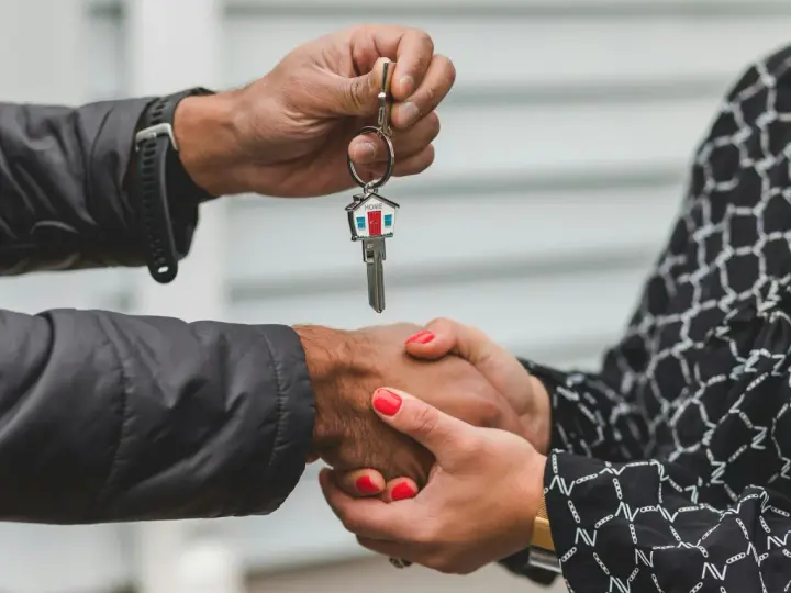 Une main tend une clé avec un porte-clés en forme de maison. Les deux mains se serrent, symbolisant la fin d'une obligation de relogement par la mairie.