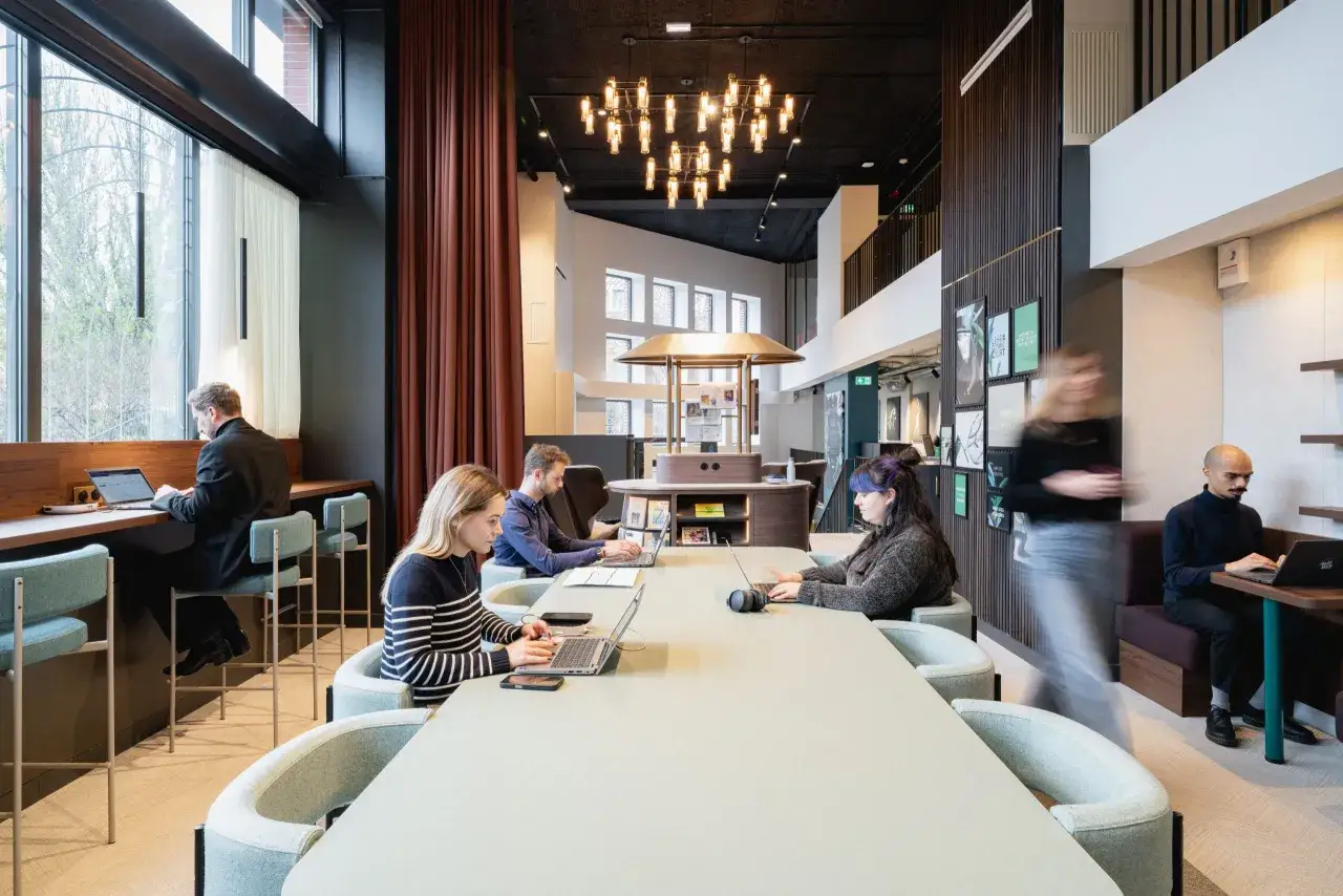 Espace de coworking moderne à Paris. Des personnes travaillent sur leurs ordinateurs portables dans un bureau lumineux avec de grandes fenêtres. Idéal pour la sous location bureaux Paris.