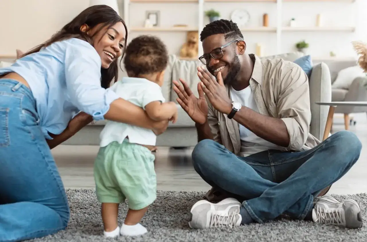 Famille jouant à claque-main avec leur bébé. Un moment de joie qui rappelle les joies du nouveau congé parental.
