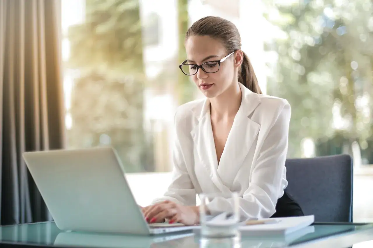 Jeune femme en télétravail à l'étranger, concentrée sur son ordinateur portable, avec une vue lumineuse sur la nature.