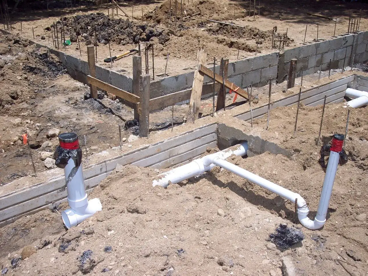 Chantier de construction avec fondations en béton et tuyaux blancs pour le tout à l'égout.
