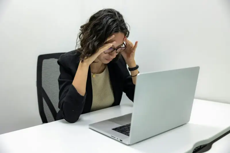 Femme stressée devant son ordinateur, les mains sur les tempes. Une situation difficile, peut-être un licenciement pendant arrêt maladie pour dépression.